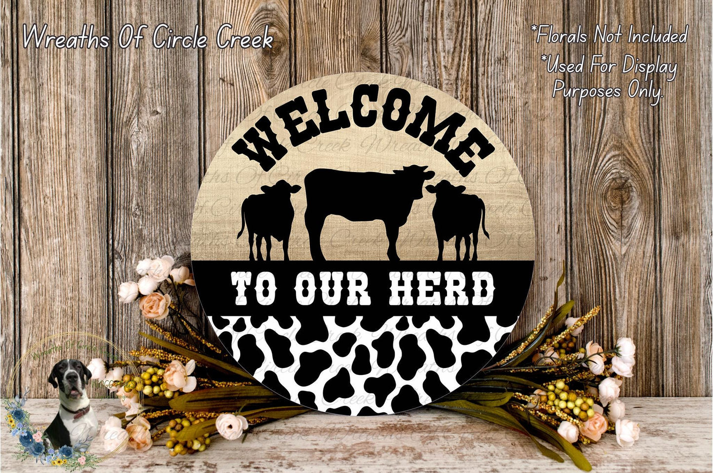 a wooden sign with the text "Welcome to our herd" and a silhouette of a cow and two cows. The sign is surrounded by flowers and placed on a wooden surface.