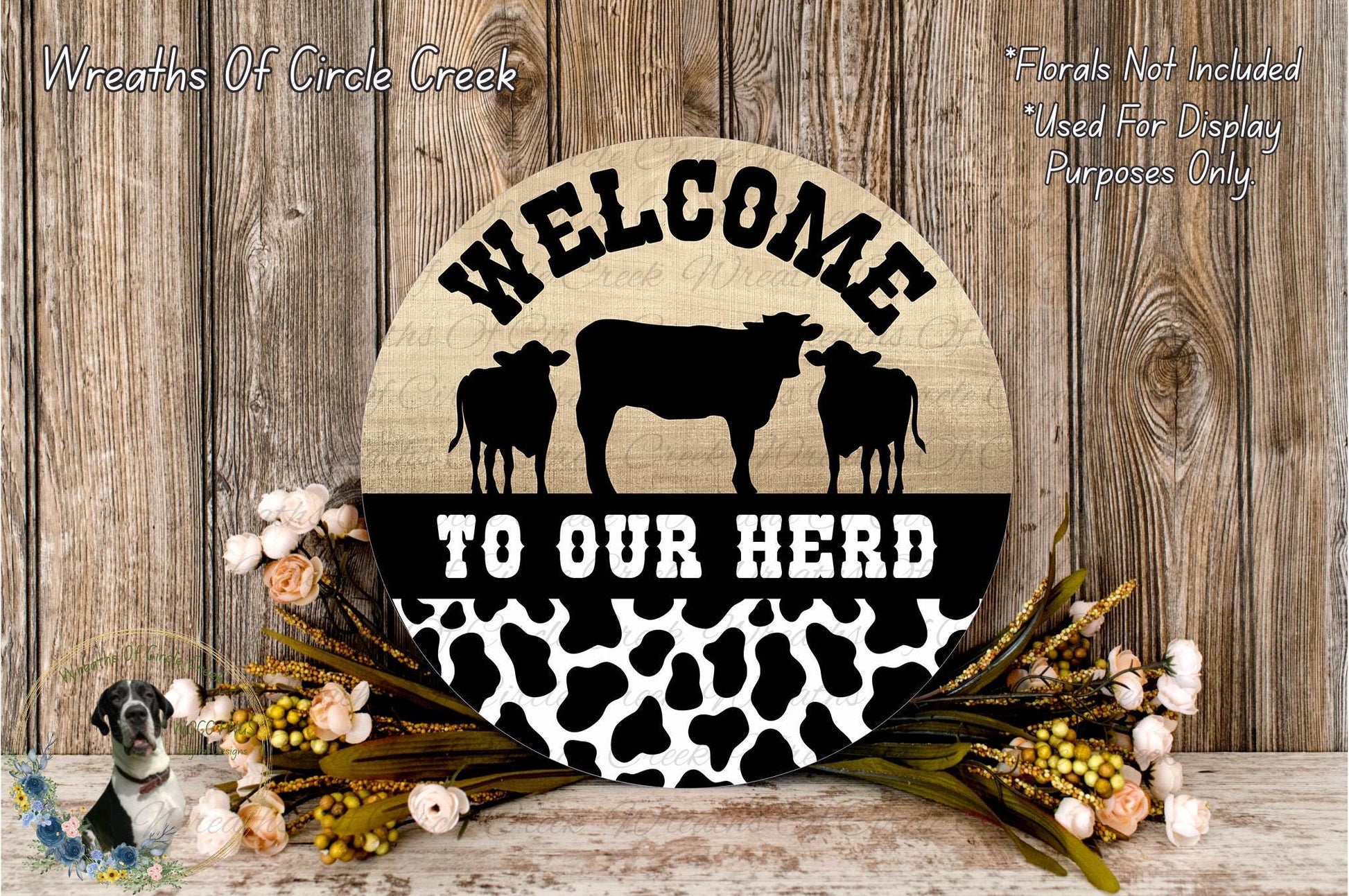a wooden sign with the text "Welcome to our herd" and a silhouette of a cow and two cows. The sign is surrounded by flowers and placed on a wooden surface.