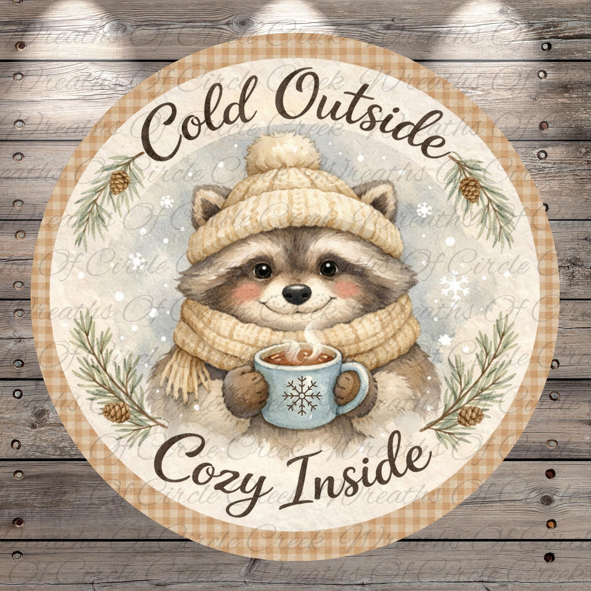 A raccoon wearing a winter hat and scarf is holding a mug of hot chocolate, surrounded by pine branches and snowflakes, with the text "Cold Outside Cozy Inside" written around the image.