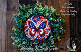 A wreath made of green leaves and a large, colorful butterfly design at the center, with a wooden background.