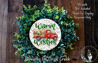 a wreath with a red truck and the text "Warm Wishes" on it, surrounded by green foliage.