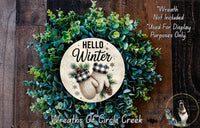 A wreath made of green leaves and pine cones, with a circular sign in the center that says "Hello Winter" and two mittens. The wreath is displayed on a wooden surface, and there is a text overlay that says "Wreath Not Included * Used For Display Purposes Only".