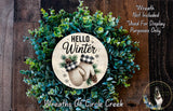 A wreath made of green leaves and pine cones, with a circular sign in the center that says "Hello Winter" and two mittens. The wreath is displayed on a wooden surface, and there is a text overlay that says "Wreath Not Included * Used For Display Purposes Only".