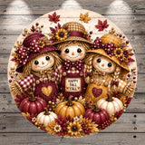 A round, decorative image featuring three scarecrow dolls surrounded by autumn-themed elements such as pumpkins, flowers, and leaves.