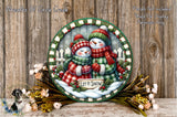 A decorative wreath featuring two snowmen wearing plaid scarves and hats, surrounded by flowers and greenery, with the text "Let it snow" on the wreath.