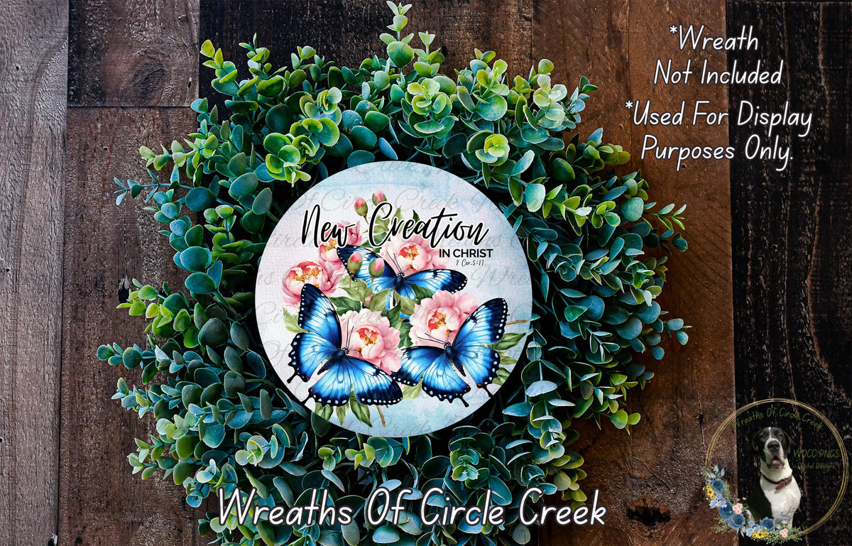 a wreath made of green leaves and flowers, with a circular design in the center that includes blue butterflies and pink flowers. The wreath is displayed on a wooden surface, and there is a small dog in the bottom right corner of the image.