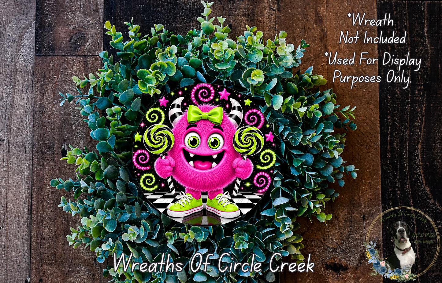 A whimsical wreath made of green leaves and flowers, featuring a large pink monster with a bow and green shoes, surrounded by a wooden background.