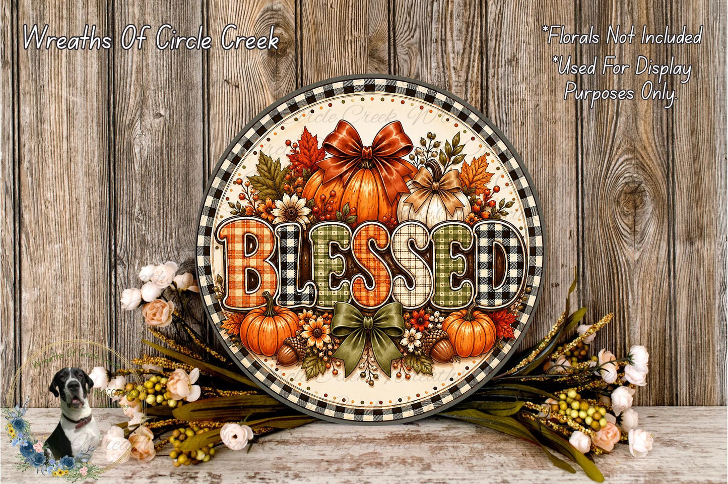 A decorative wreath with the word "Blessed" written on it, surrounded by autumn-themed elements such as pumpkins, leaves, and flowers. The wreath is displayed on a wooden surface, with a floral arrangement and some flowers nearby.