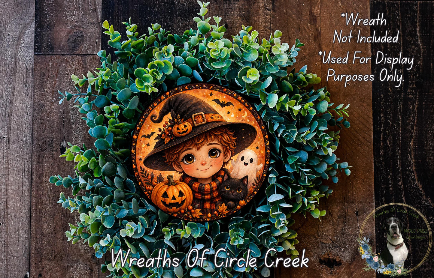 A Halloween-themed wreath featuring a young girl in a witch's hat, a pumpkin, and a cat, surrounded by green foliage.
