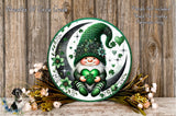 A decorative plate featuring a gnome wearing a green hat and holding a green heart, surrounded by flowers and a crescent moon.