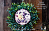 A wreath made of green leaves and a purple and white teddy bear holding a heart-shaped envelope, with the text "Sending You Love" on the wreath.
