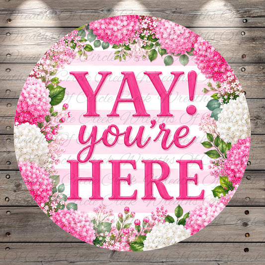 A circular sign with the text "YAY! you're here" surrounded by pink flowers and greenery.
