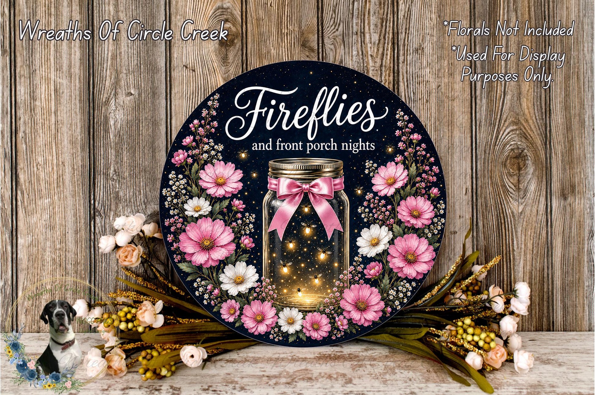 a decorative wreath with a jar of fireflies, surrounded by pink and white flowers, placed on a wooden surface.
