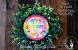 A wreath made of green leaves and featuring a colorful sign that says "Snow Cones Ice Cold".