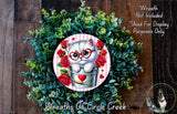 A wreath made of green leaves and red roses, with a small white cat wearing glasses and a heart-shaped bell around its neck, surrounded by a circular design with a heart and a rose.