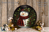 A snowman wearing a red and black plaid scarf and a black top hat, surrounded by holly and berries, with a wreath of flowers and a bird in the background.