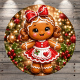 A cheerful, glittery gingerbread girl with a red bow on her head is surrounded by Christmas decorations, including berries, holly leaves, and ornaments, all set against a blurred background of twinkling lights.