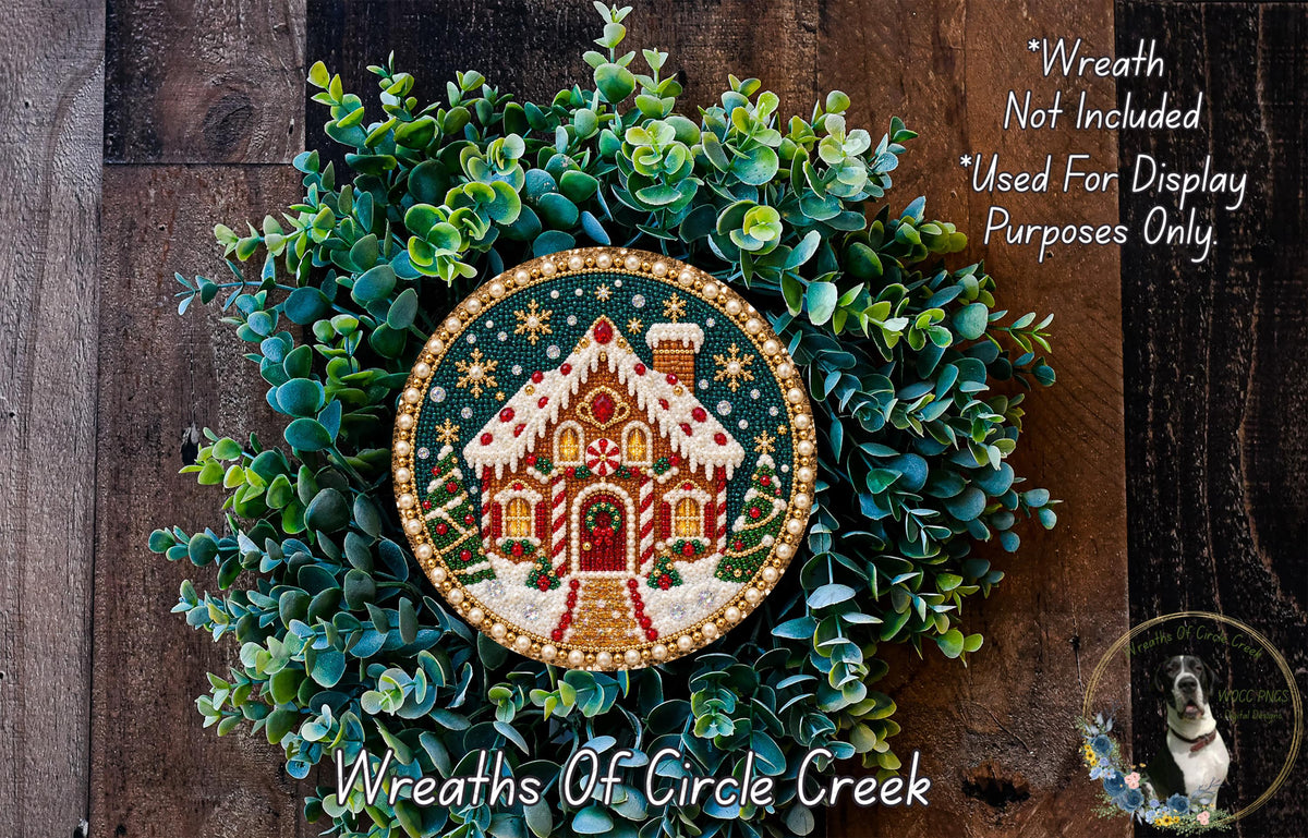 A wreath made of green leaves and a circular ornament featuring a gingerbread house design, with a wooden background.