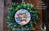 a wreath made of various green plants and flowers, with a circular design in the center that says "Home Sweet Home".