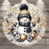 A snowman wearing a black and gold hat and scarf, surrounded by a wreath of snowflakes, pine cones, and other winter decorations, all set against a wooden background.