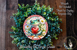 A wreath featuring a frog holding a heart, surrounded by green foliage and flowers.