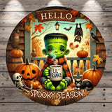 A spooky illustration featuring a green-skinned, green-haired monster holding a mug with the text "Lil' Frankie" and surrounded by Halloween-themed elements such as pumpkins, bats, and a skeleton.