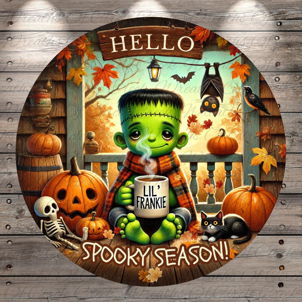 A spooky illustration featuring a green-skinned, green-haired monster holding a mug with the text "Lil' Frankie" and surrounded by Halloween-themed elements such as pumpkins, bats, and a skeleton.