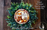 A wreath made of green foliage and featuring a fox wearing a sweater and holding a pumpkin, with the text "I love warmer weather" and "I love sweaters" written on it.
