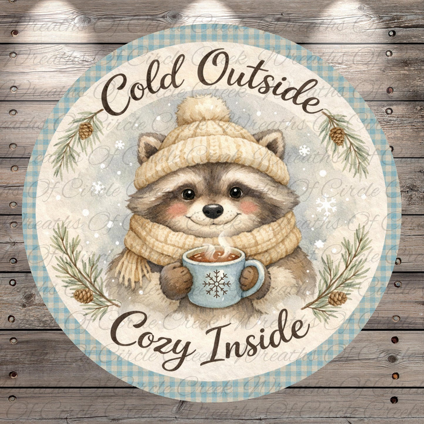 A raccoon wearing a winter hat and scarf is holding a mug of hot chocolate, surrounded by pine branches and snowflakes, with the text "Cold Outside Cozy Inside" written around the image.