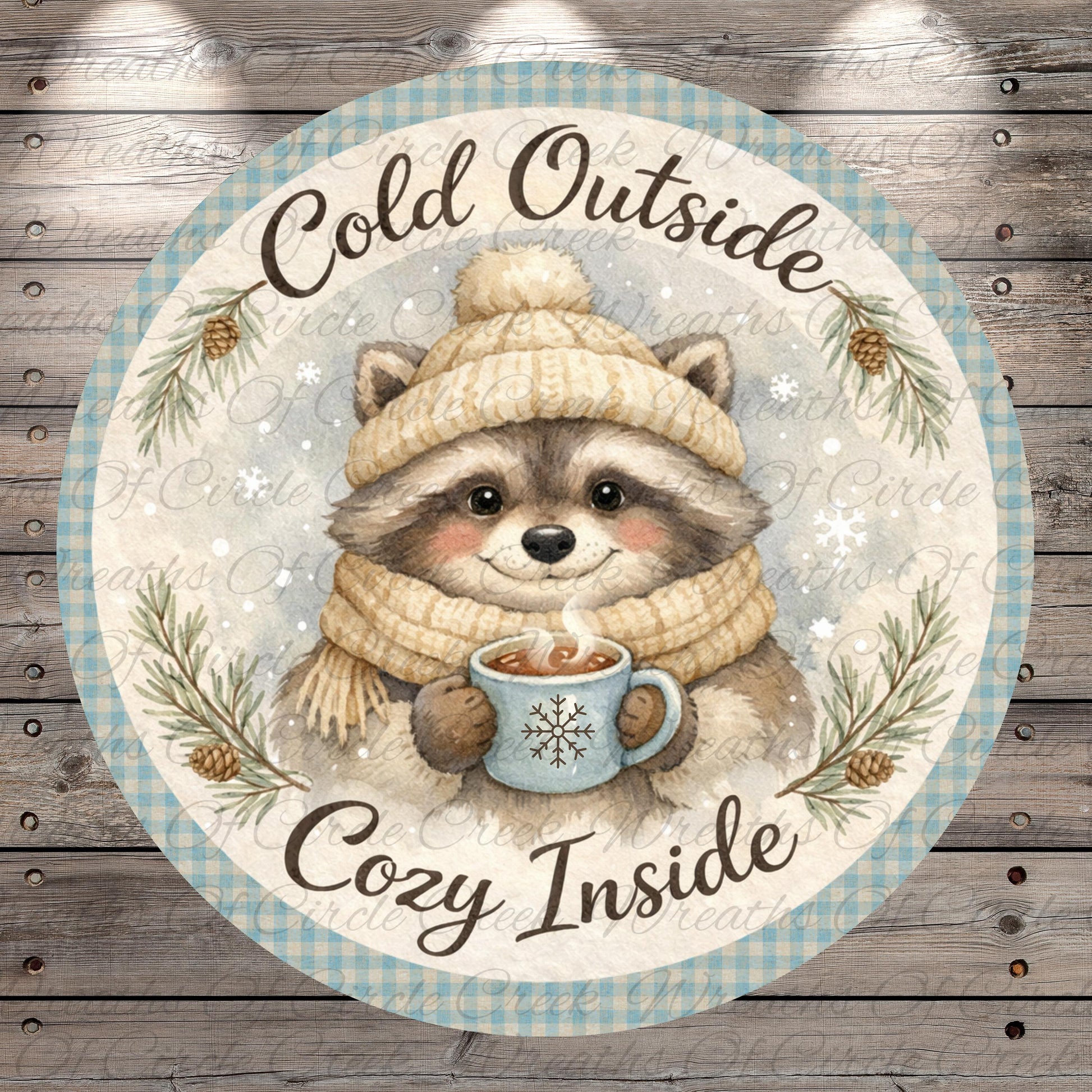 A raccoon wearing a winter hat and scarf is holding a mug of hot chocolate, surrounded by pine branches and snowflakes, with the text "Cold Outside Cozy Inside" written around the image.