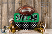 A wooden sign with the text "game day" and a football on it, surrounded by a floral arrangement and a wooden wall.