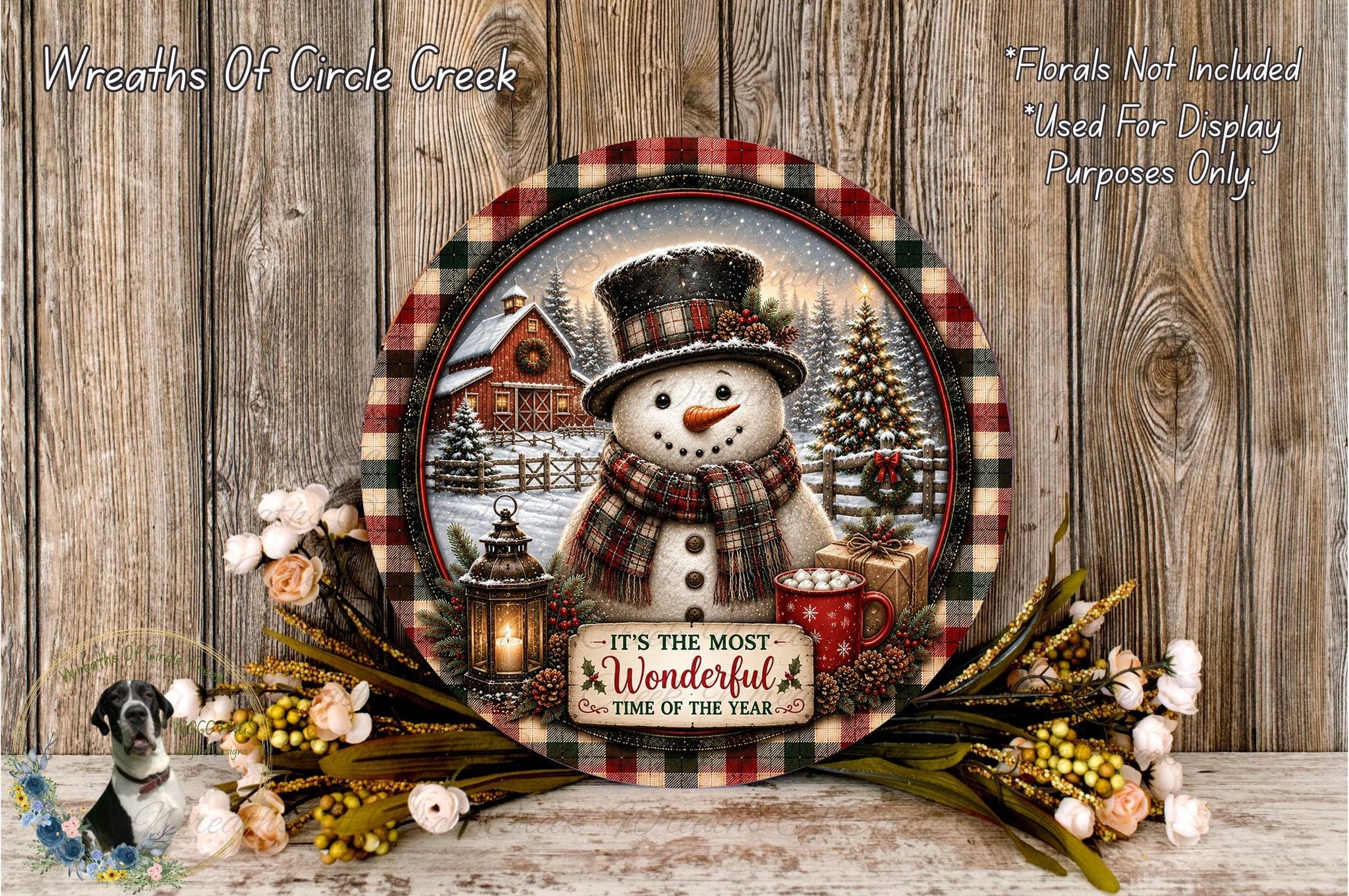 A decorative snowman with a lantern, a red mug, and a sign that says "It's the most wonderful time of the year" is displayed on a wooden surface, surrounded by flowers and greenery.
