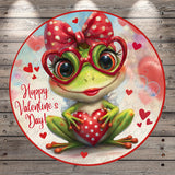 A cheerful green frog wearing red polka dot glasses and holding a red heart, surrounded by red hearts, with the text "Happy Valentine's Day!" displayed.