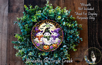 A Halloween-themed wreath made of green foliage and featuring three small, whimsical characters dressed in costumes.