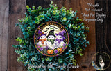 A Halloween-themed wreath made of green foliage and featuring three small, whimsical characters dressed in costumes.
