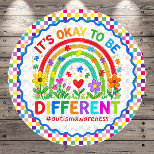 The image is a colorful, circular sign with a rainbow and flowers, along with the text "It's OKAY TO BE DIFFERENT #autismawareness".