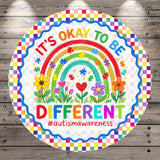 The image is a colorful, circular sign with a rainbow and flowers, along with the text "It's OKAY TO BE DIFFERENT #autismawareness".
