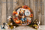 A wreath with a teddy bear wearing a plaid sweater and holding a cup of coffee, surrounded by autumn decorations such as pumpkins, leaves, and flowers, all set against a wooden background.