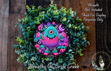 A wreath made of green plants and featuring a colorful, whimsical monster with a pink and blue body, surrounded by stars and other decorative elements.