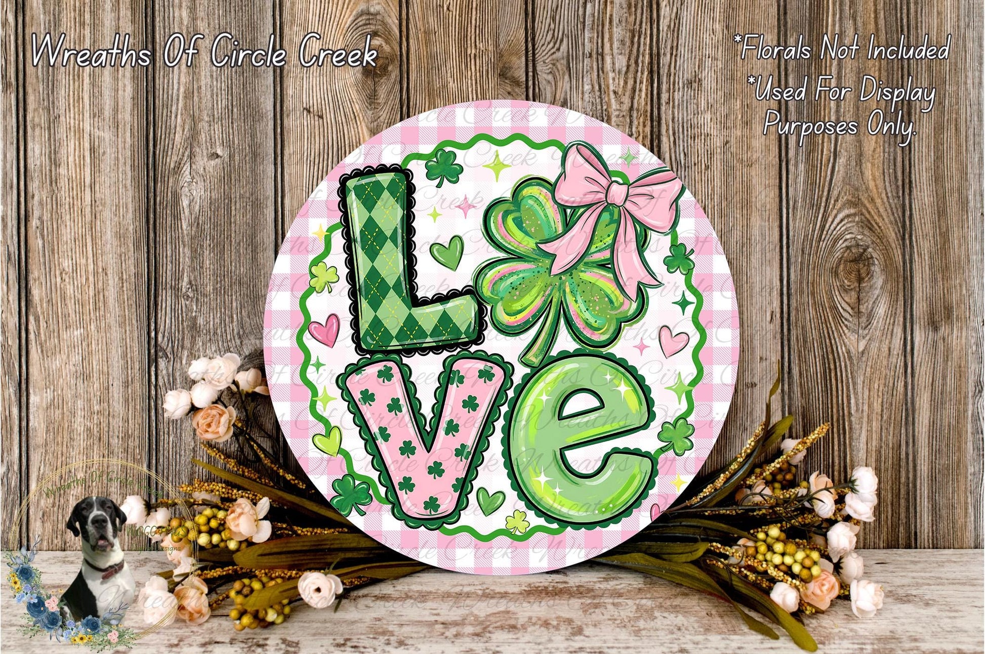 A decorative sign with the word "Love" in large letters, surrounded by various floral elements such as clovers, hearts, and flowers. The sign is placed on a wooden surface, and there are additional floral elements in the background.