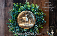 A wreath made of green foliage and a glass snow globe with a ballerina figure inside, set against a wooden background.