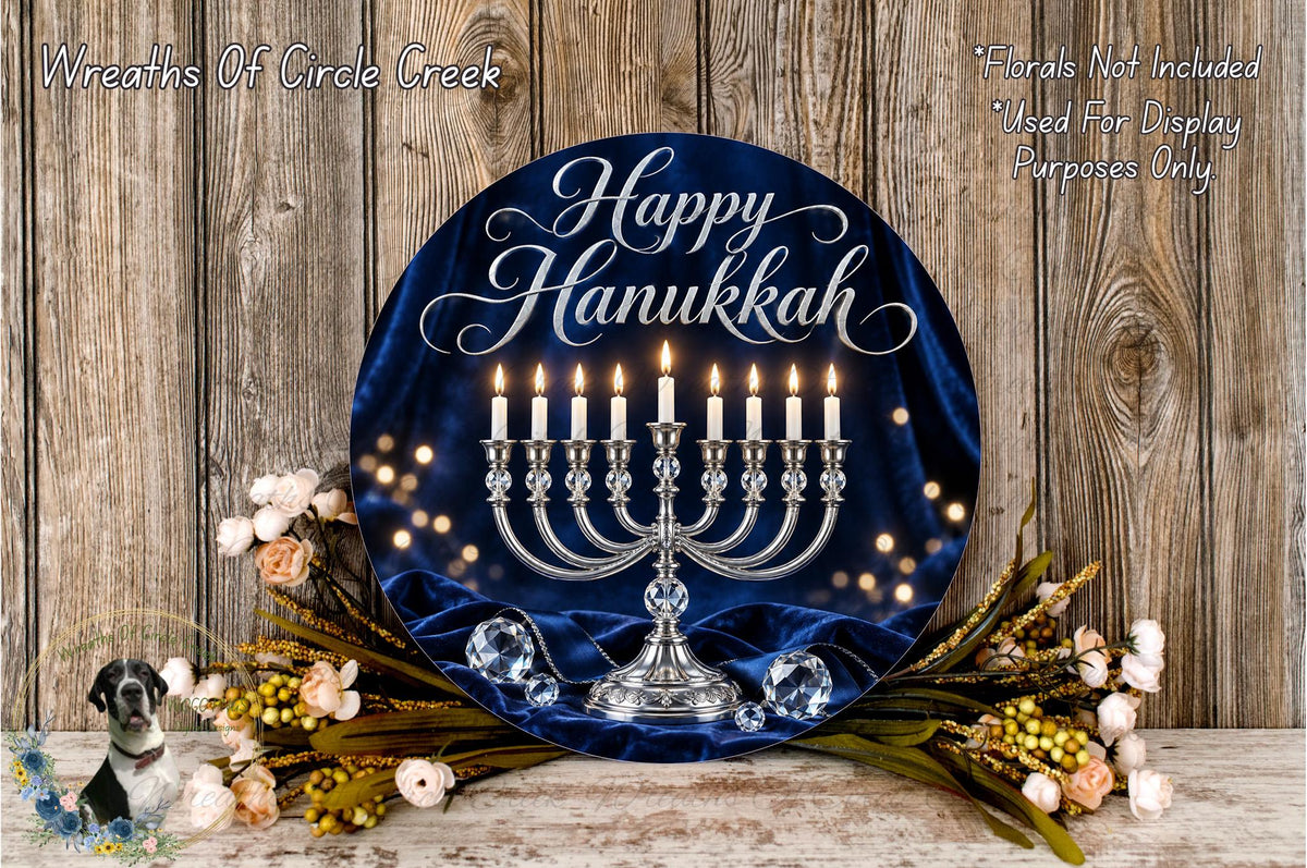 A round blue wreath with a silver menorah and lit candles, surrounded by flowers and greenery, against a wooden background.