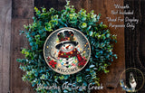 A wreath with a snowman and the word "WELCOME" on it, surrounded by greenery.