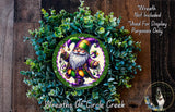 a wreath with a gnome figure in the center, surrounded by a lush green plant. The wreath is displayed on a wooden surface, and there is a small dog visible in the bottom right corner of the image.