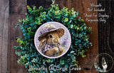 A wreath featuring a rabbit wearing a hat and holding flowers, surrounded by a lush green plant.