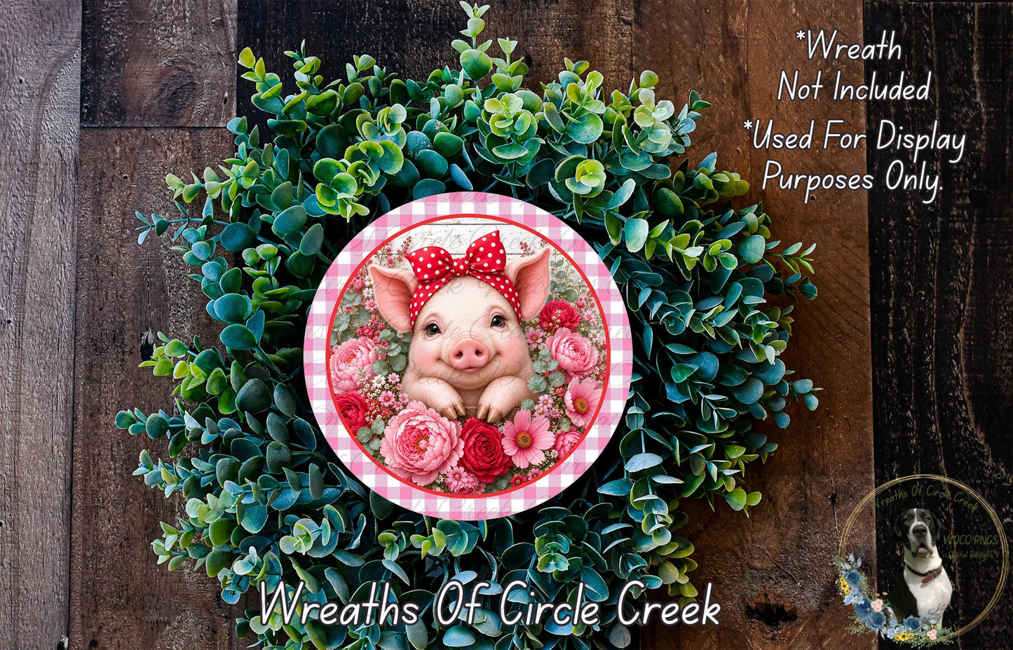 A wreath made of green foliage and pink flowers, with a pig wearing a red bow on top. The wreath is displayed on a wooden surface, and there is a text overlay that reads "Wreath Not Included * Used For Display Purposes Only".