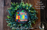 a wreath made of green leaves and a colorful sign that reads "Fight for Autism Awareness" in the center. The wreath is displayed on a wooden surface, and there is a small dog in the bottom right corner of the image.