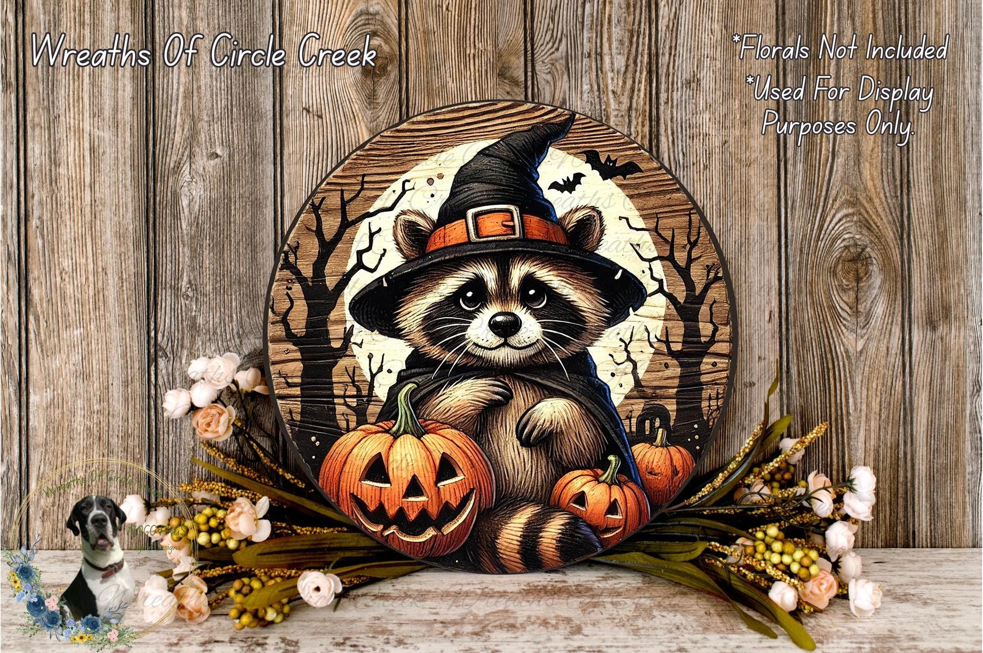 A Halloween-themed wreath featuring a raccoon wearing a witch's hat, holding carved pumpkins, and surrounded by flowers and a full moon.