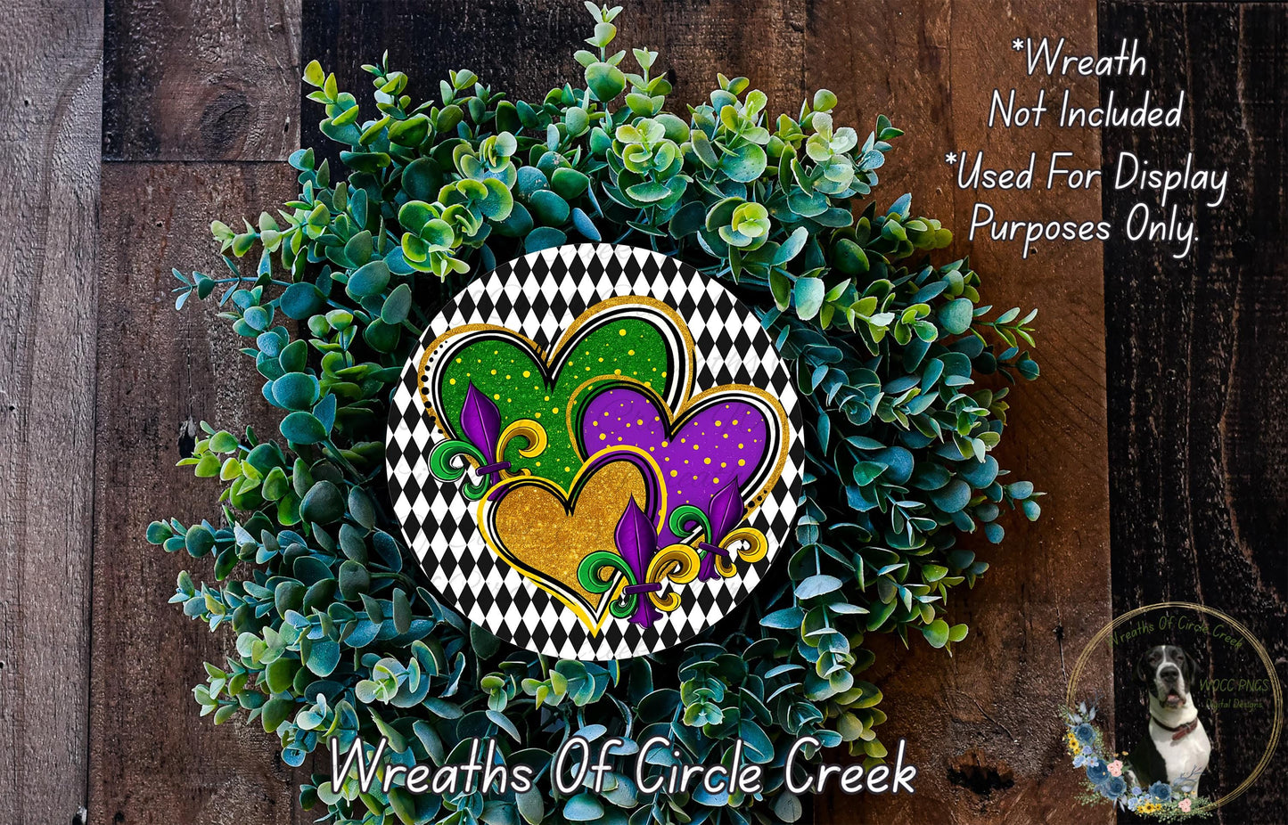a wreath made of green and purple flowers, with a heart-shaped design in the center. The wreath is displayed on a wooden surface, and there is a small dog in the bottom right corner of the image.