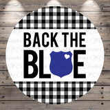 a circular design with a black and white checkered pattern and a blue shield with a heart symbol in the center. The text "BACK THE BLUE" is prominently displayed in the center of the design.